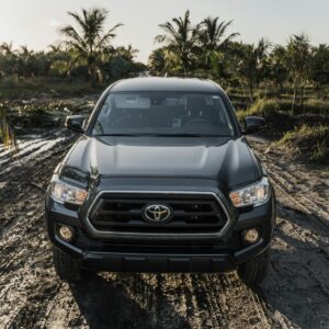Front view of a Toyota Tacoma navigating a rugged dirt road in a tropical landscape during daytime.